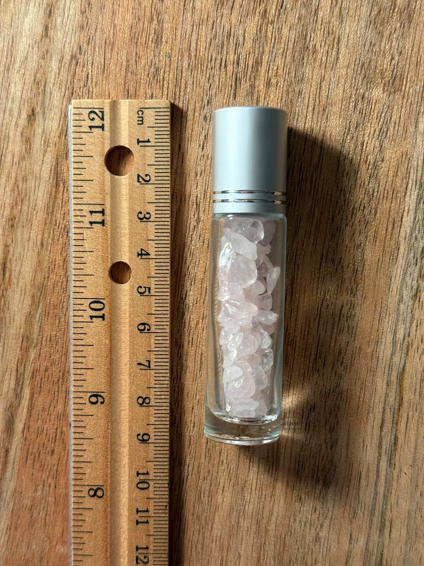 Small glass bottle with Crystal Rose Quartz next to a wooden ruler on a wooden surface