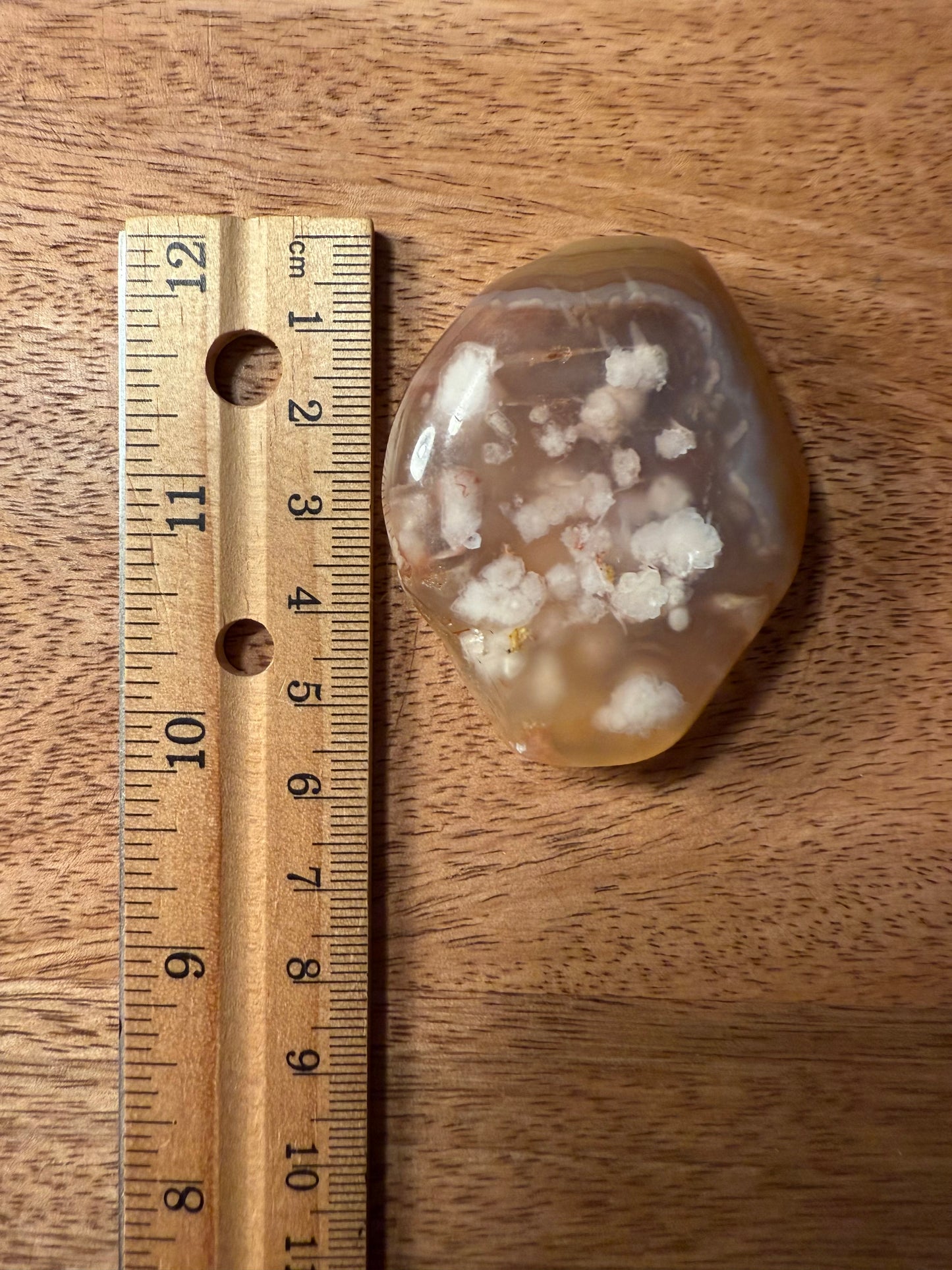 Sakura (Cherry Blossom) Agate stone with embedded white crystals next to a wooden ruler on a wooden surface