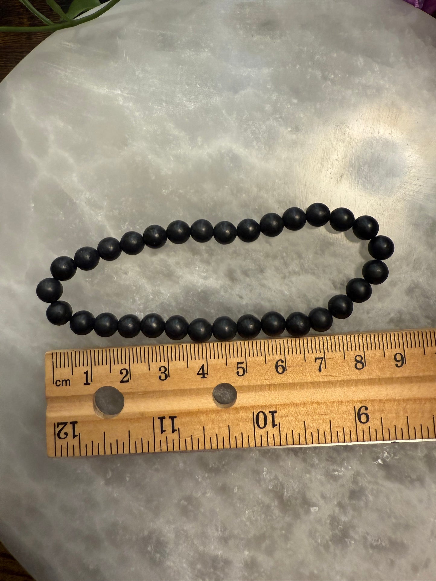 Black Natural Shungite Bead Bracelet on a wooden ruler for scale on a gray surface