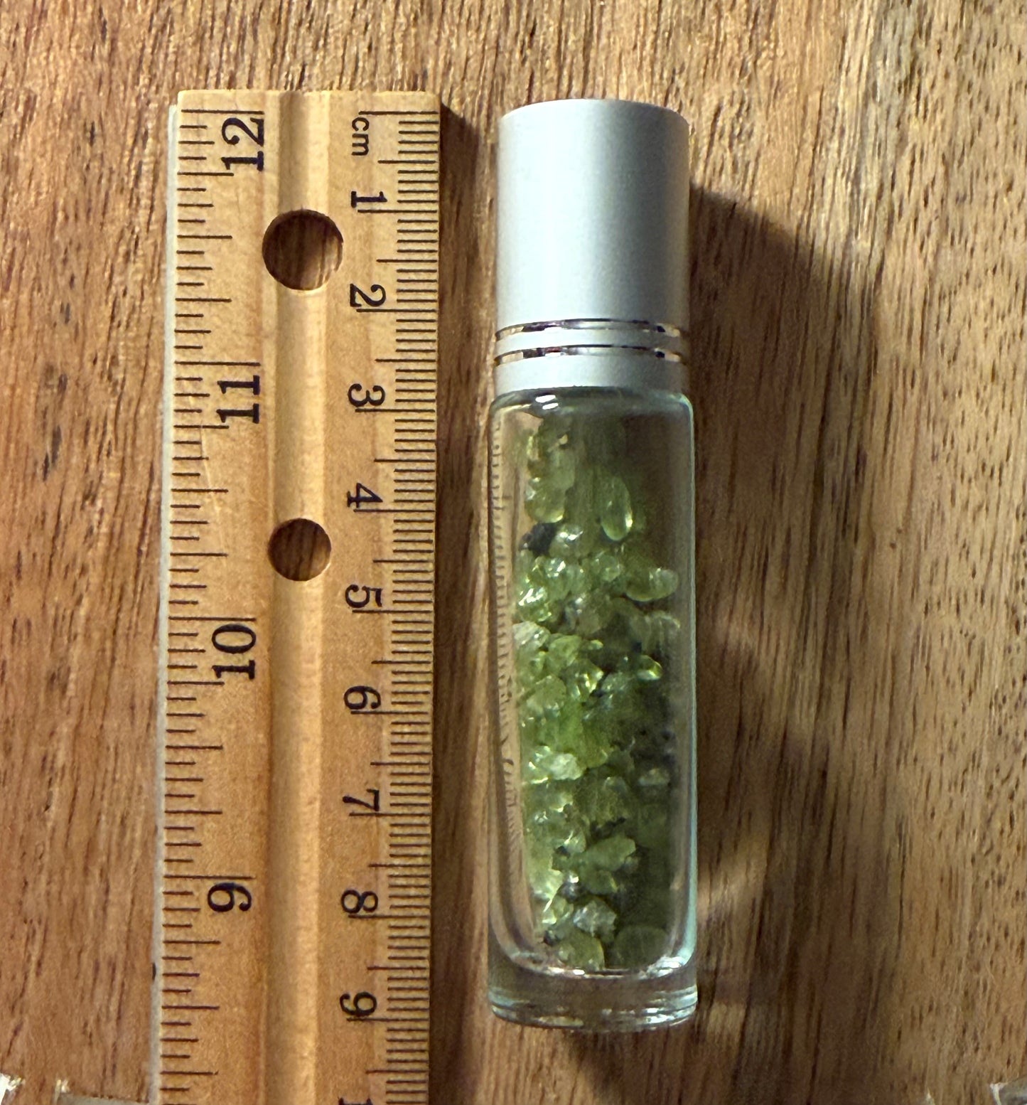 Glass bottle with green stones next to a wooden ruler on a wooden surface