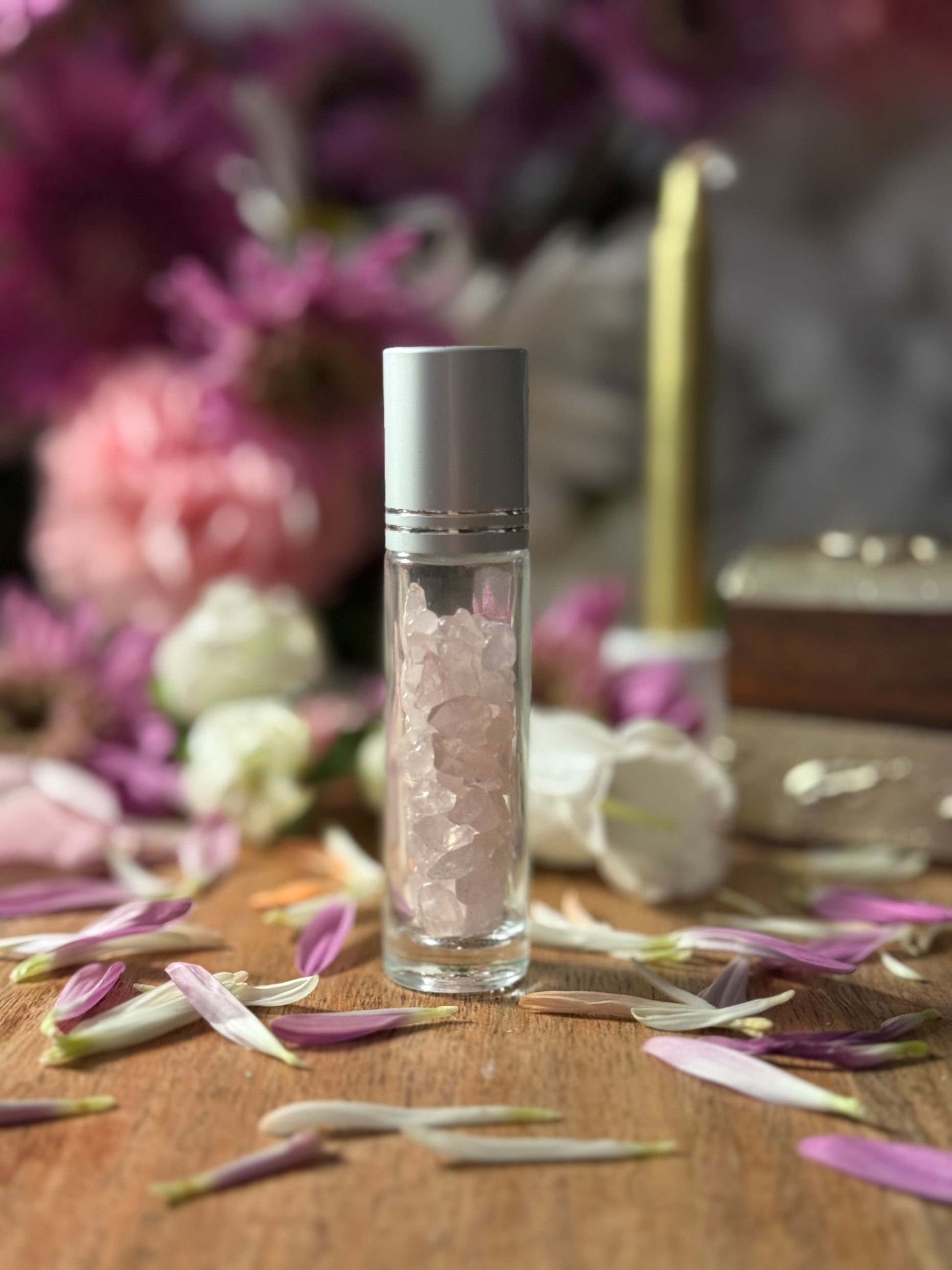 Glass bottle with Crystal Rose Quartz content on a wooden surface with flowers and a candle in the background