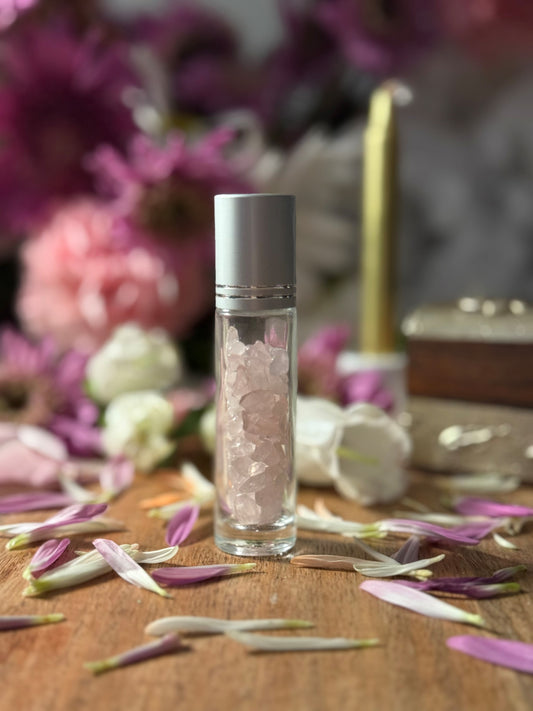 Glass bottle with Crystal Rose Quartz content on a wooden surface with flowers and a candle in the background