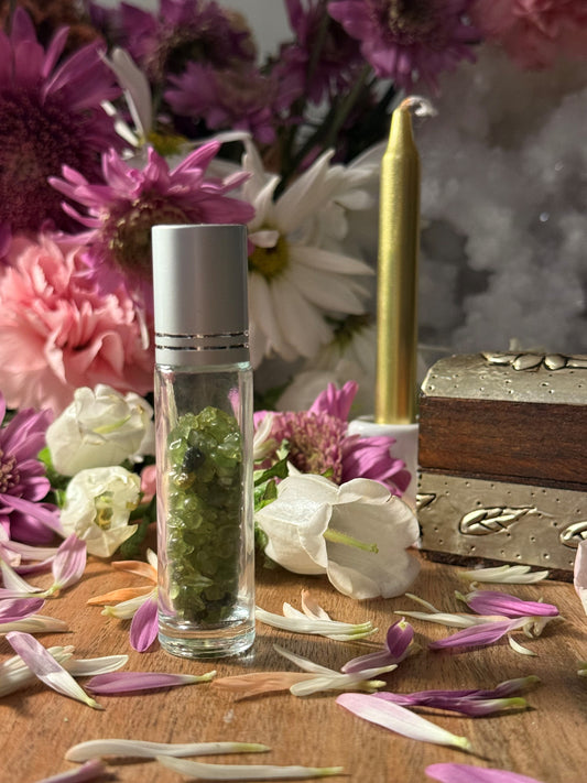 Glass container with green stones on a wooden surface with flowers and a candle in the background