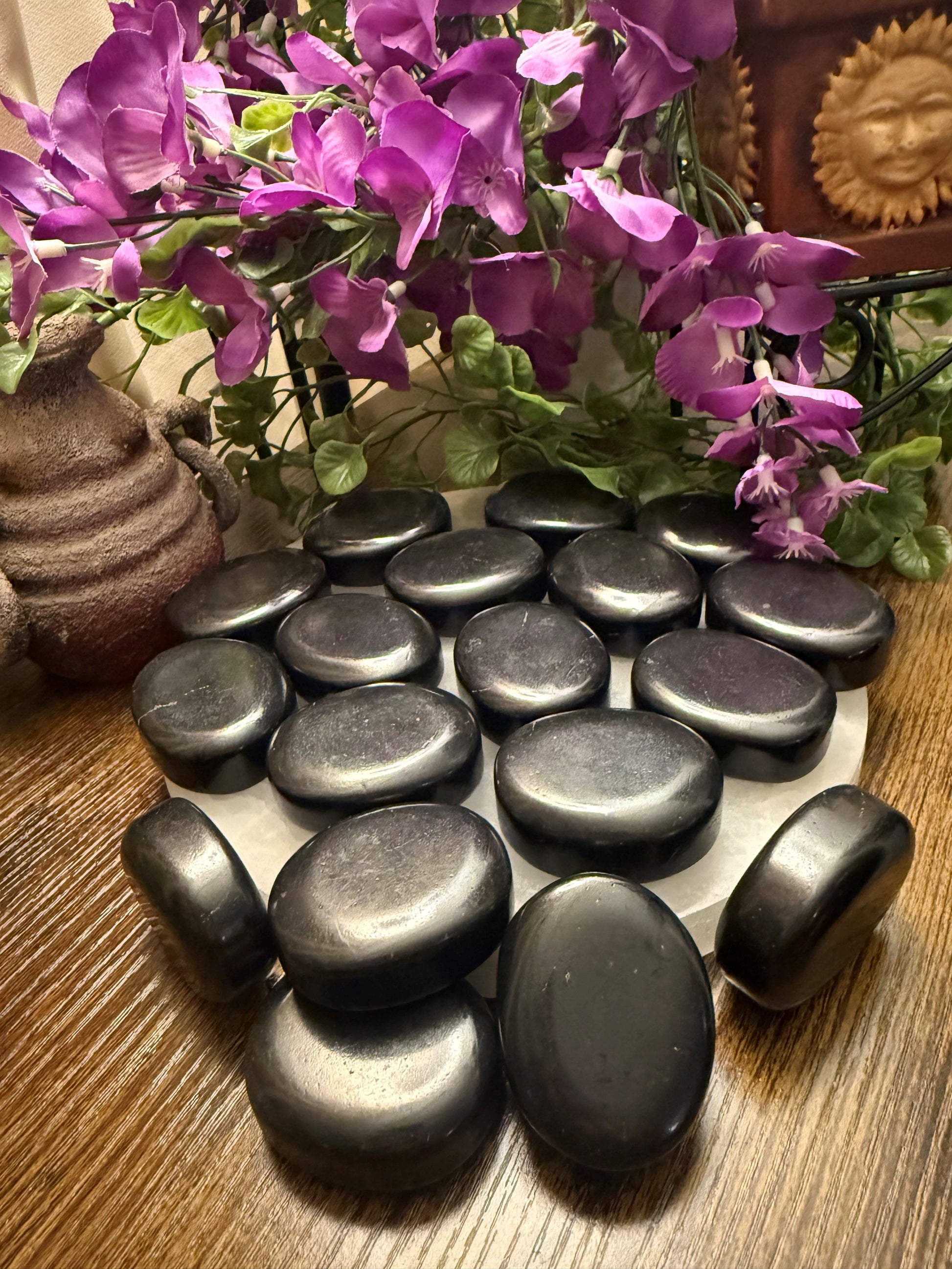 Set of black stones on a wooden surface with purple flowers in the background
