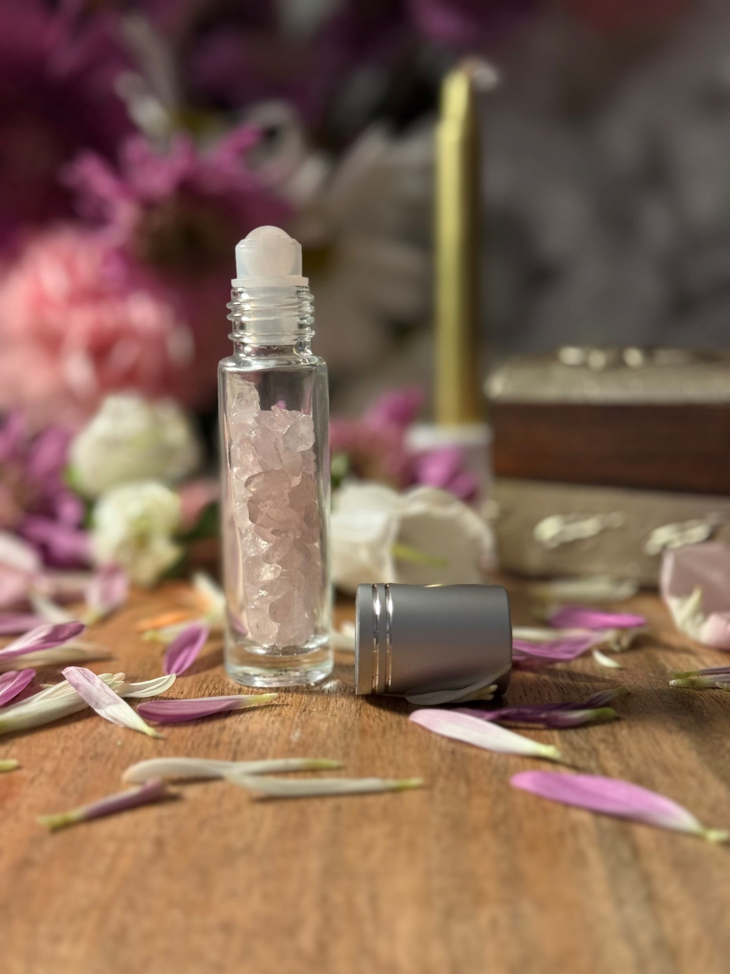 Roll-on bottle with Crystal Rose Quartz on a wooden surface with flowers and a gold box in the background