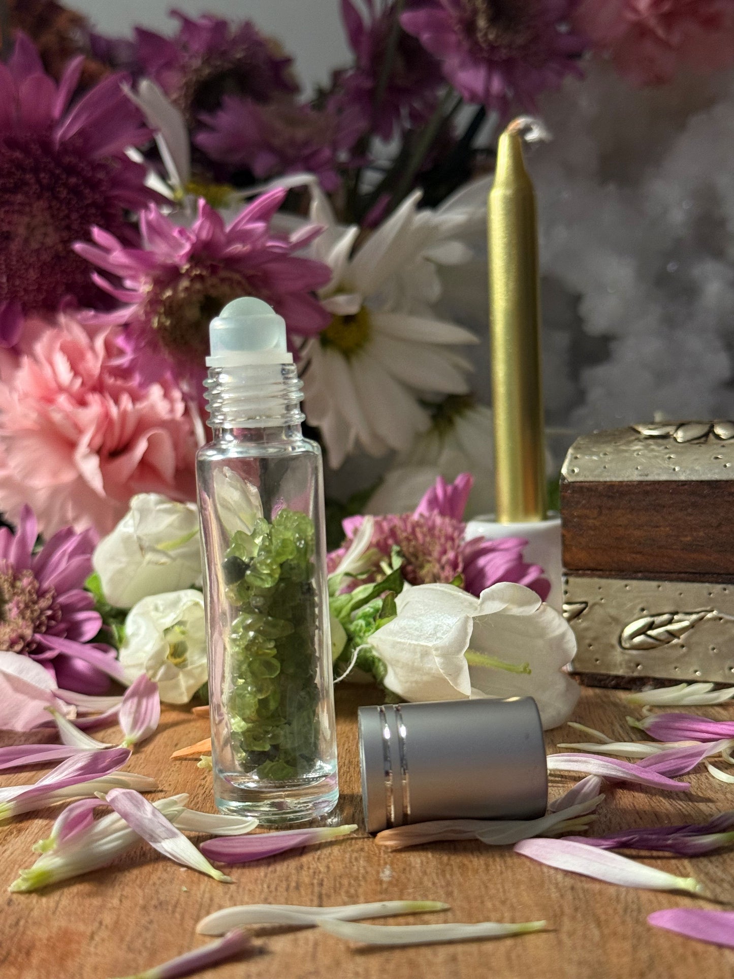 Roll-on bottle with green stones surrounded by flowers and a wooden box on a wooden surface.