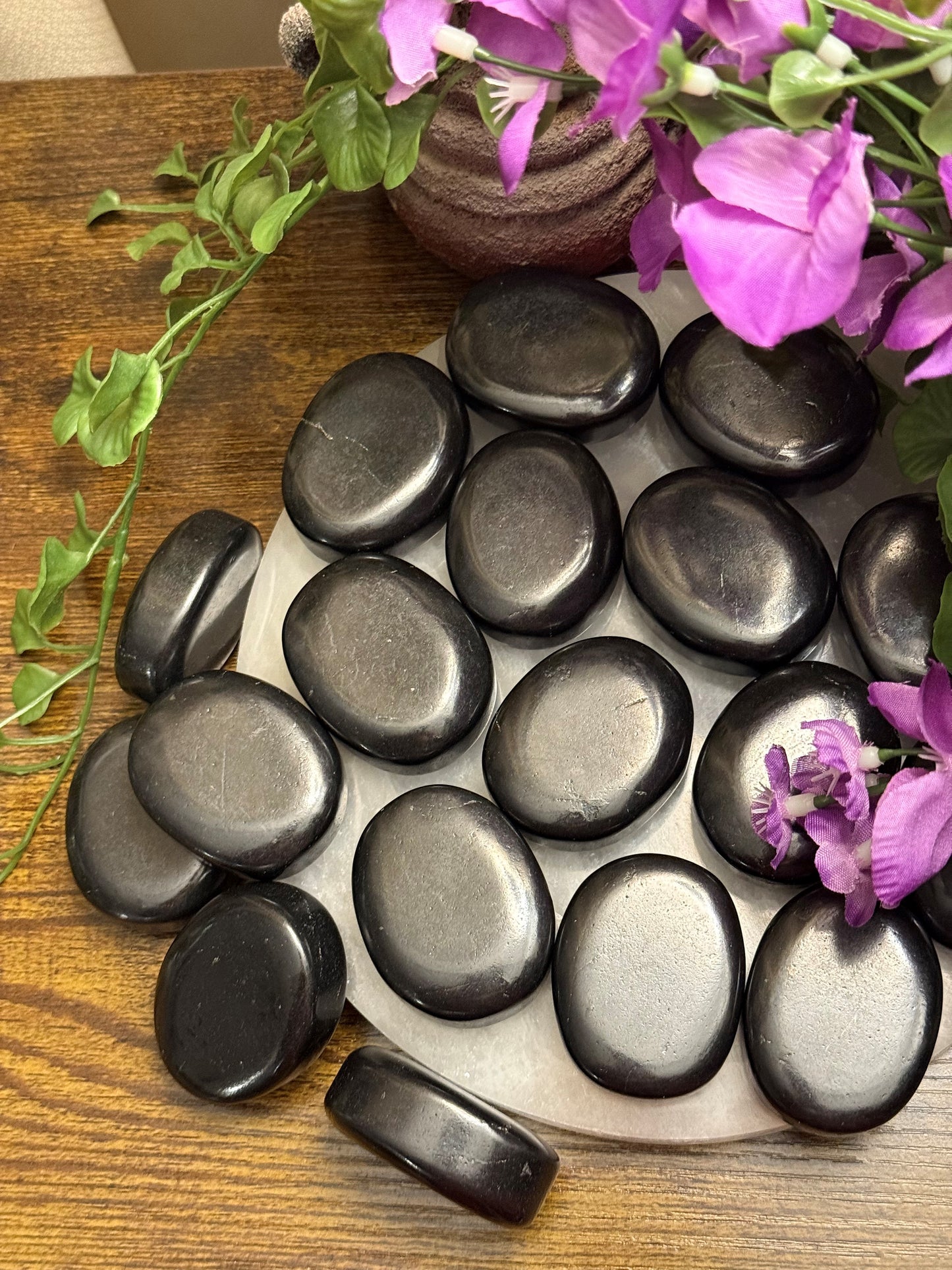 Set of black stones on a white plate with purple flowers and green leaves on a wooden surface