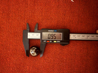 Digital caliper measuring a Black Magnetic Hematite Spheres on a red textured background