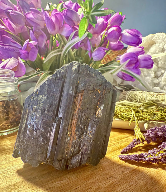 Raw Black Tourmaline on a wooden surface with purple flowers in the background