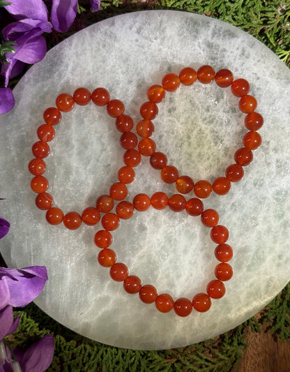 Red Carnelian beaded bracelets on a white stone with purple flowers in the background