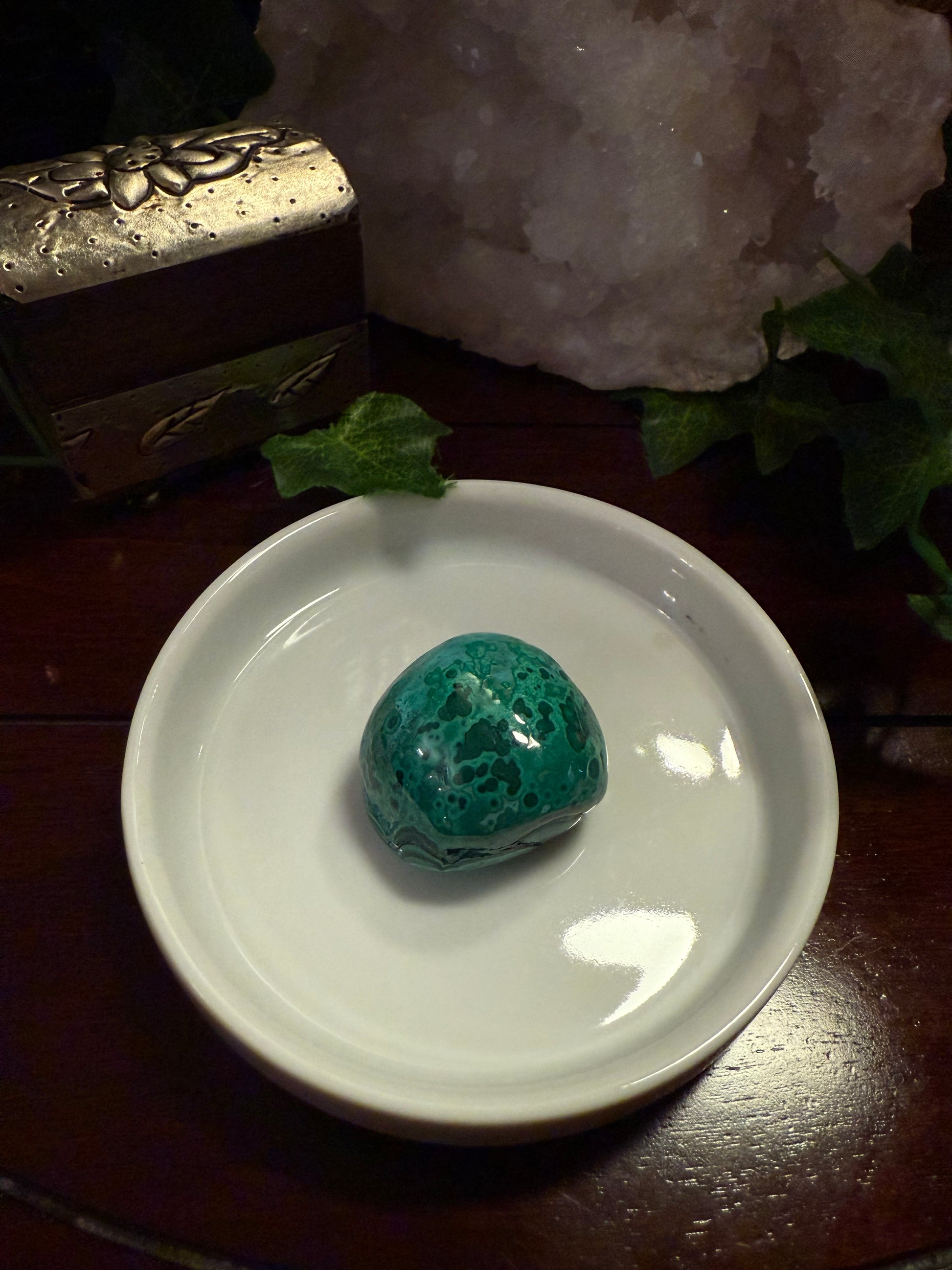 Turquoise stone on a white dish with a decorative box and crystal in the background