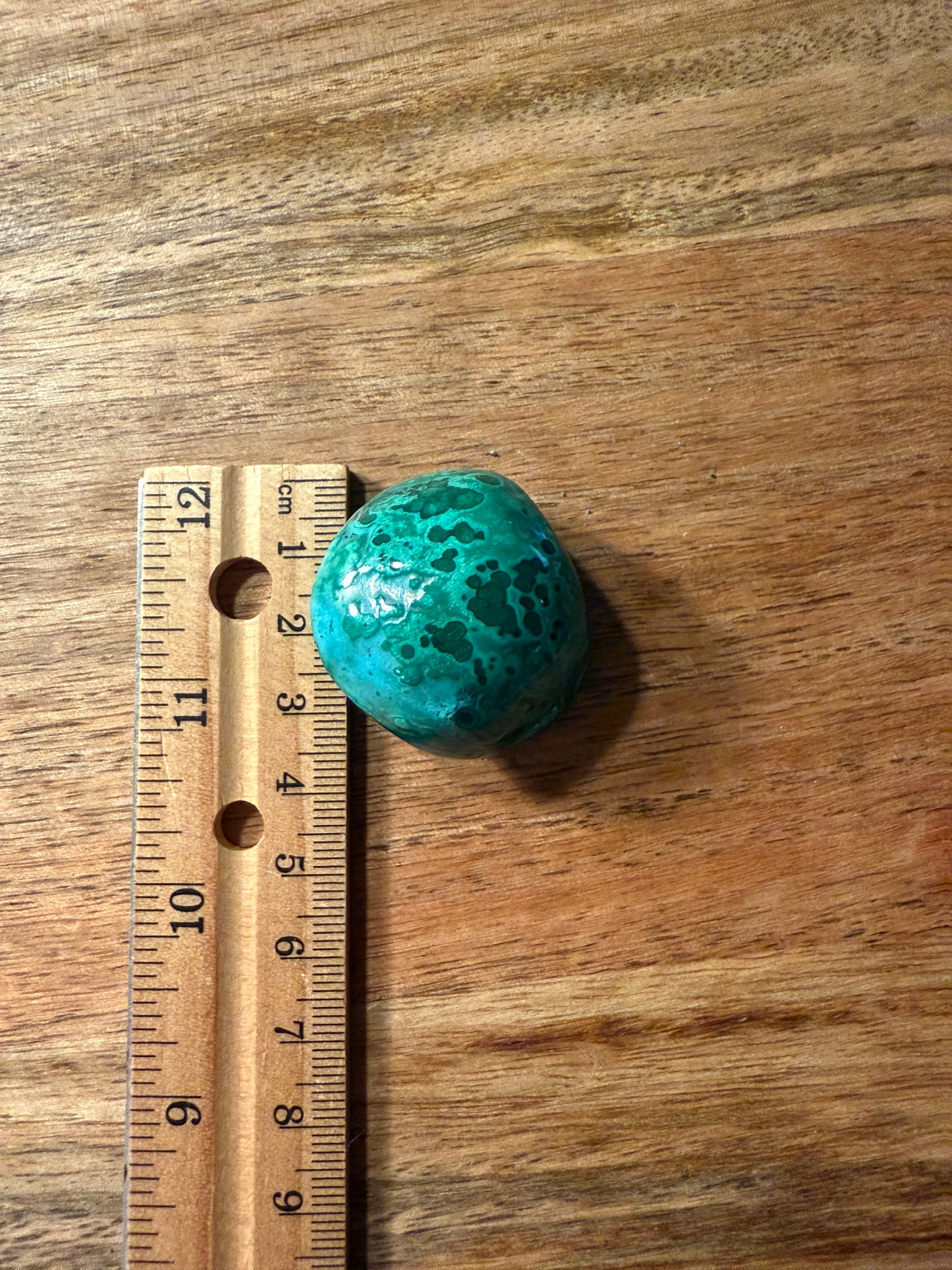 Turquoise stone next to a wooden ruler on a wooden surface