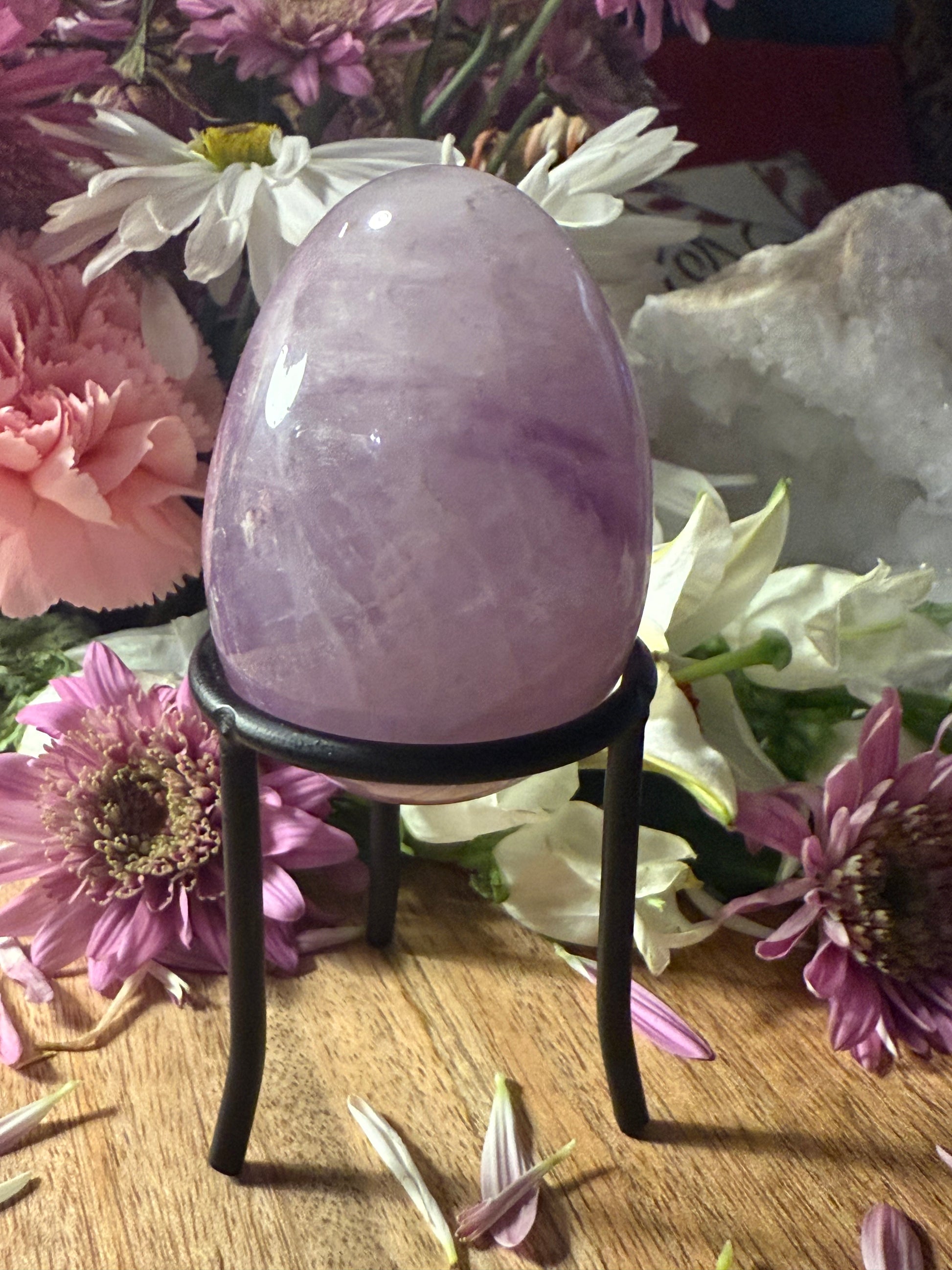 Crystal egg on a stand surrounded by flowers and crystals