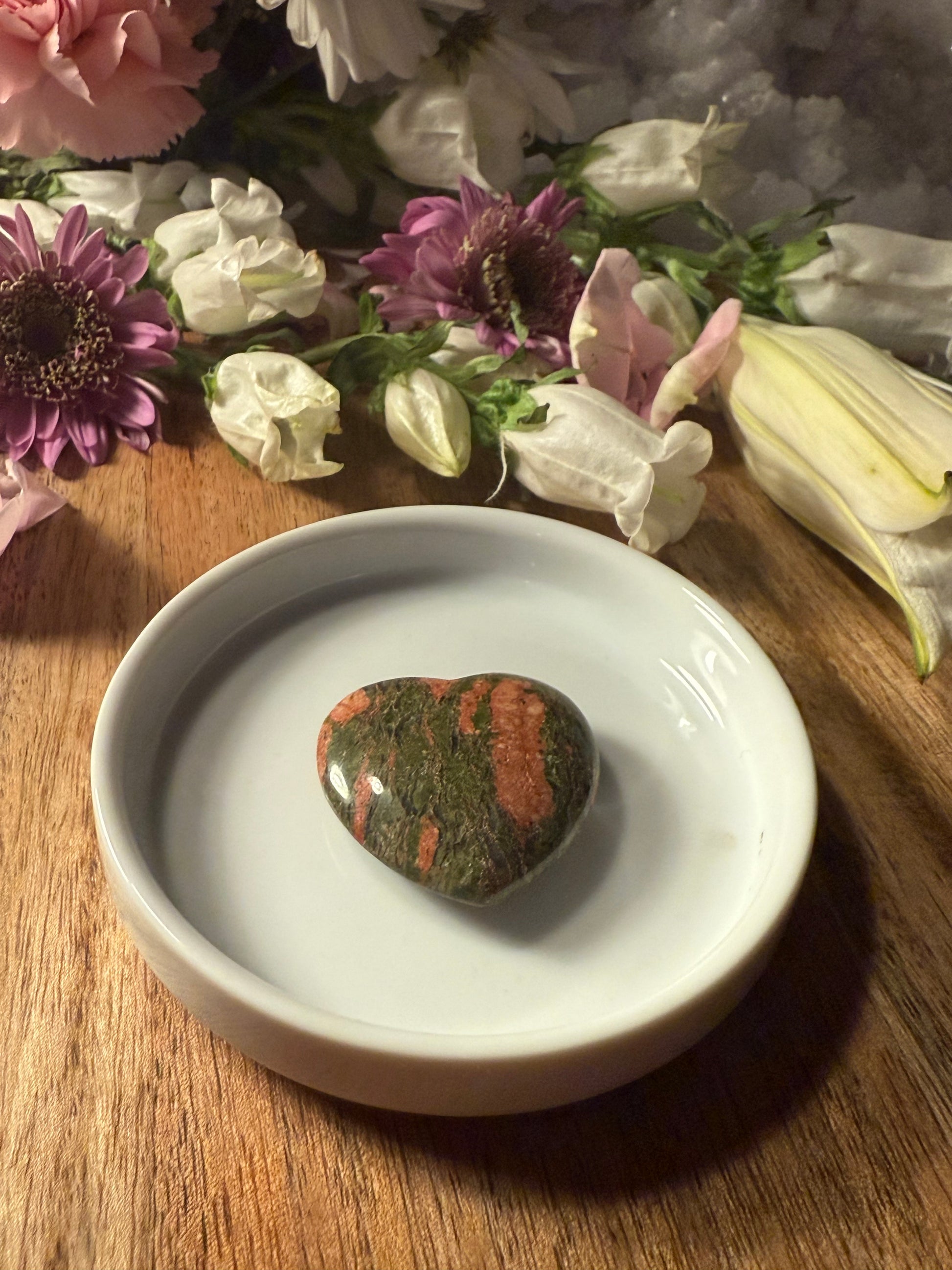 Unakite Crystal Heart stone on a white dish with flowers in the background