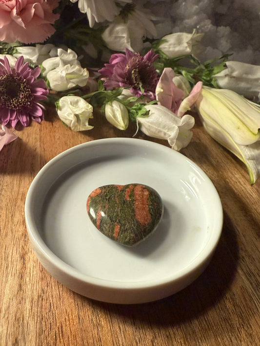 Unakite Crystal Heart stone on a white dish with flowers in the background
