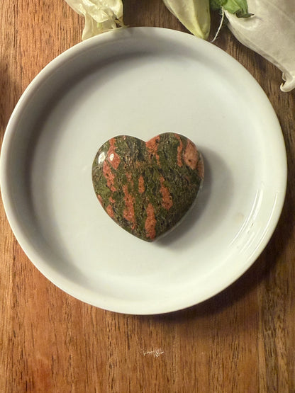 Unakite Crystal Heart stone on a white plate with a wooden background