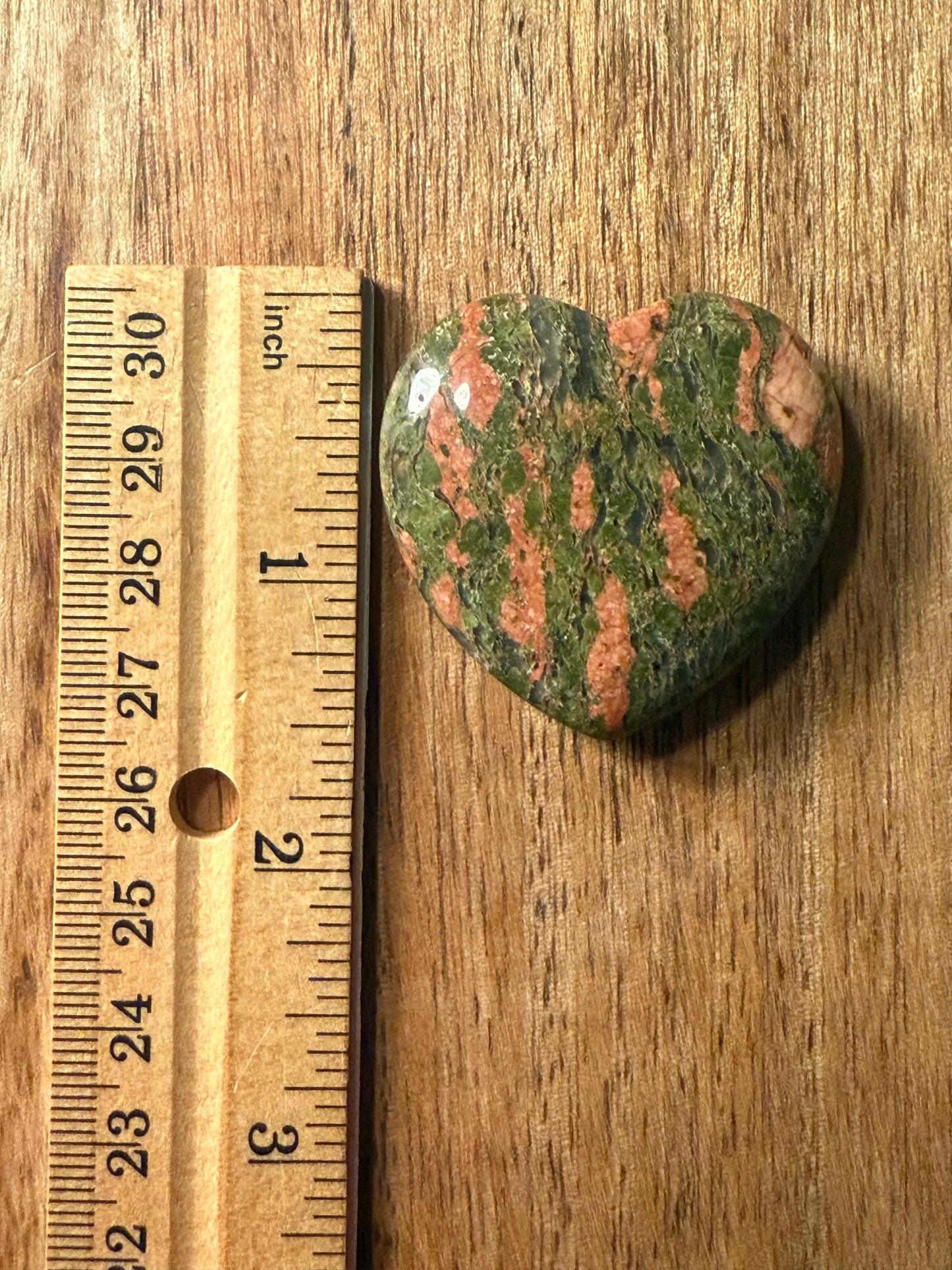 Polished Unakite Crystal Heart stone next to a wooden ruler on a wooden surface