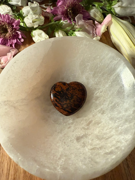 Mahogany Obsidian Crystal Heart stone on a white stone surface with flowers in the background