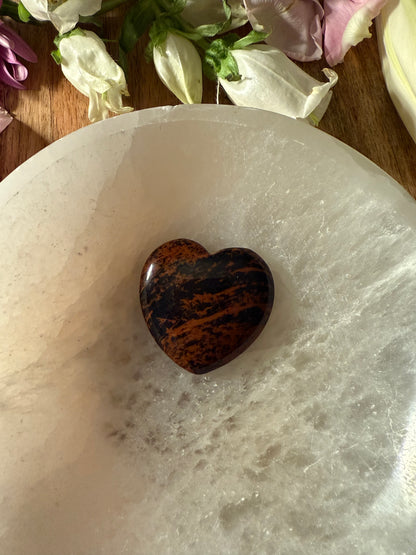 Mahogany Obsidian Crystal Heart stone on a white marble surface with flowers in the background