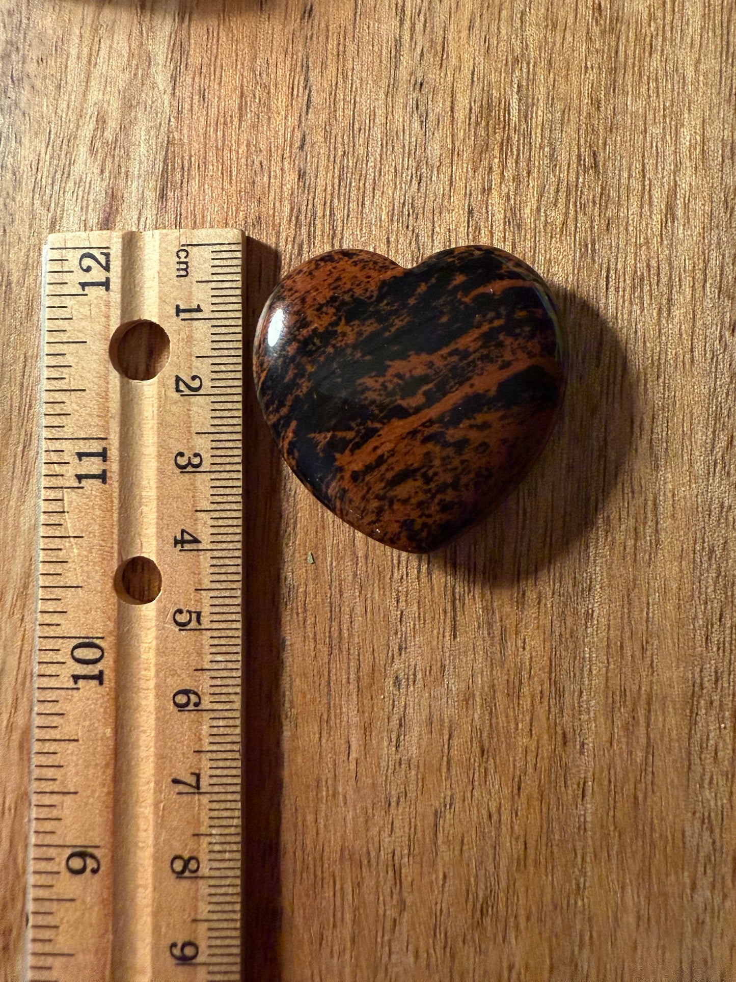 Mahogany Obsidian Crystal Heart stone next to a wooden ruler on a wooden surface