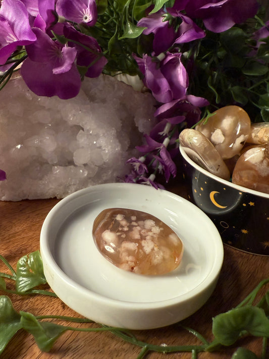 Sakura (Cherry Blossom) Agate stone on a white dish with purple flowers and a crystal in the background