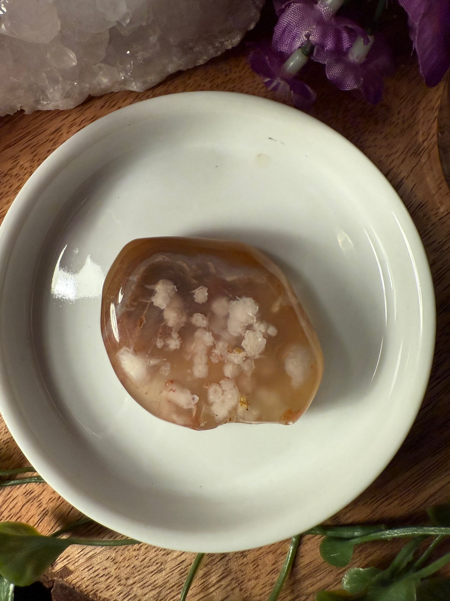 Sakura (Cherry Blossom) Agate stone on a white dish with purple flowers and a crystal in the background