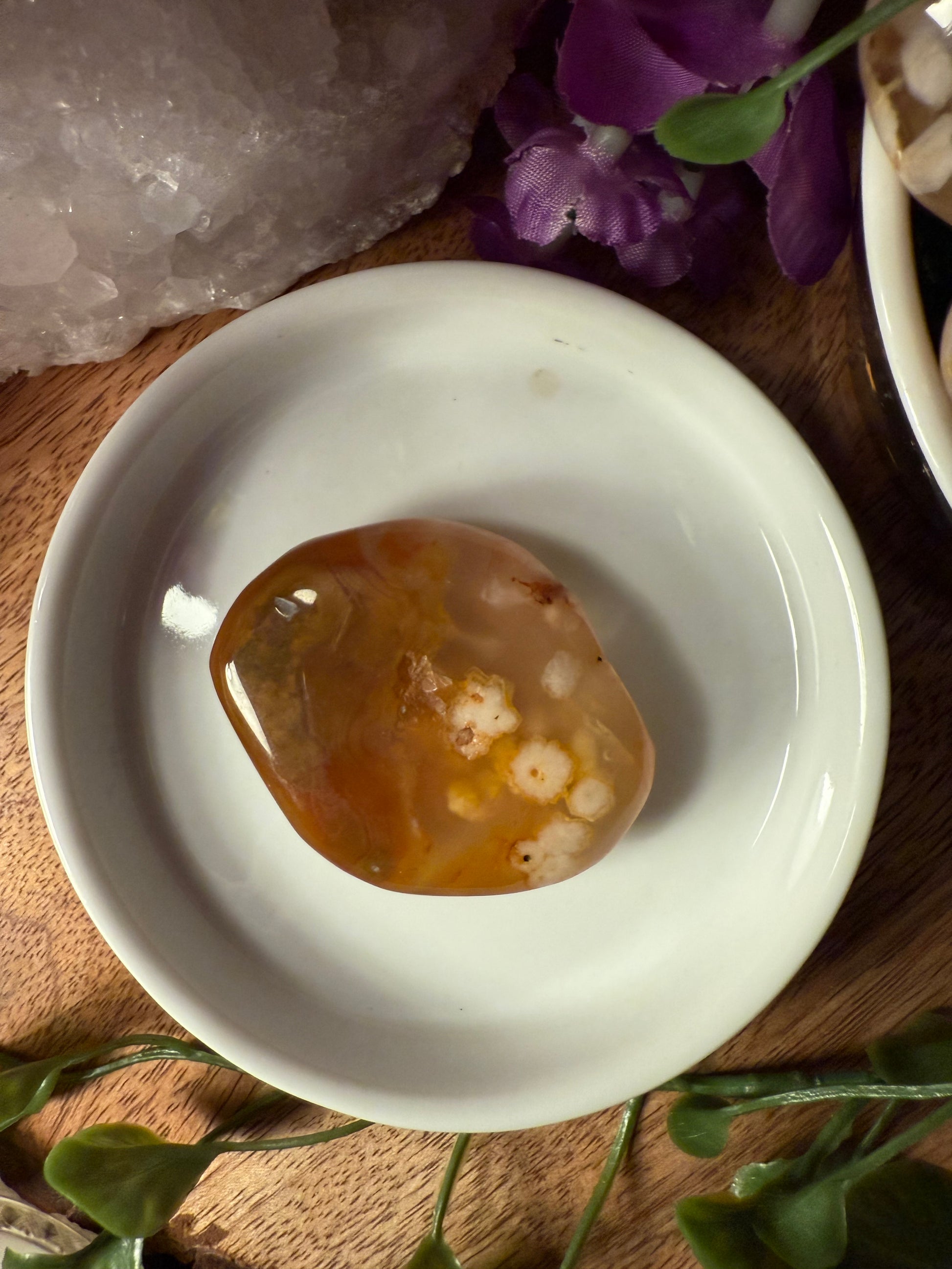 Small dish with a Sakura (Cherry Blossom) Agate stone on a wooden surface with flowers and crystals.