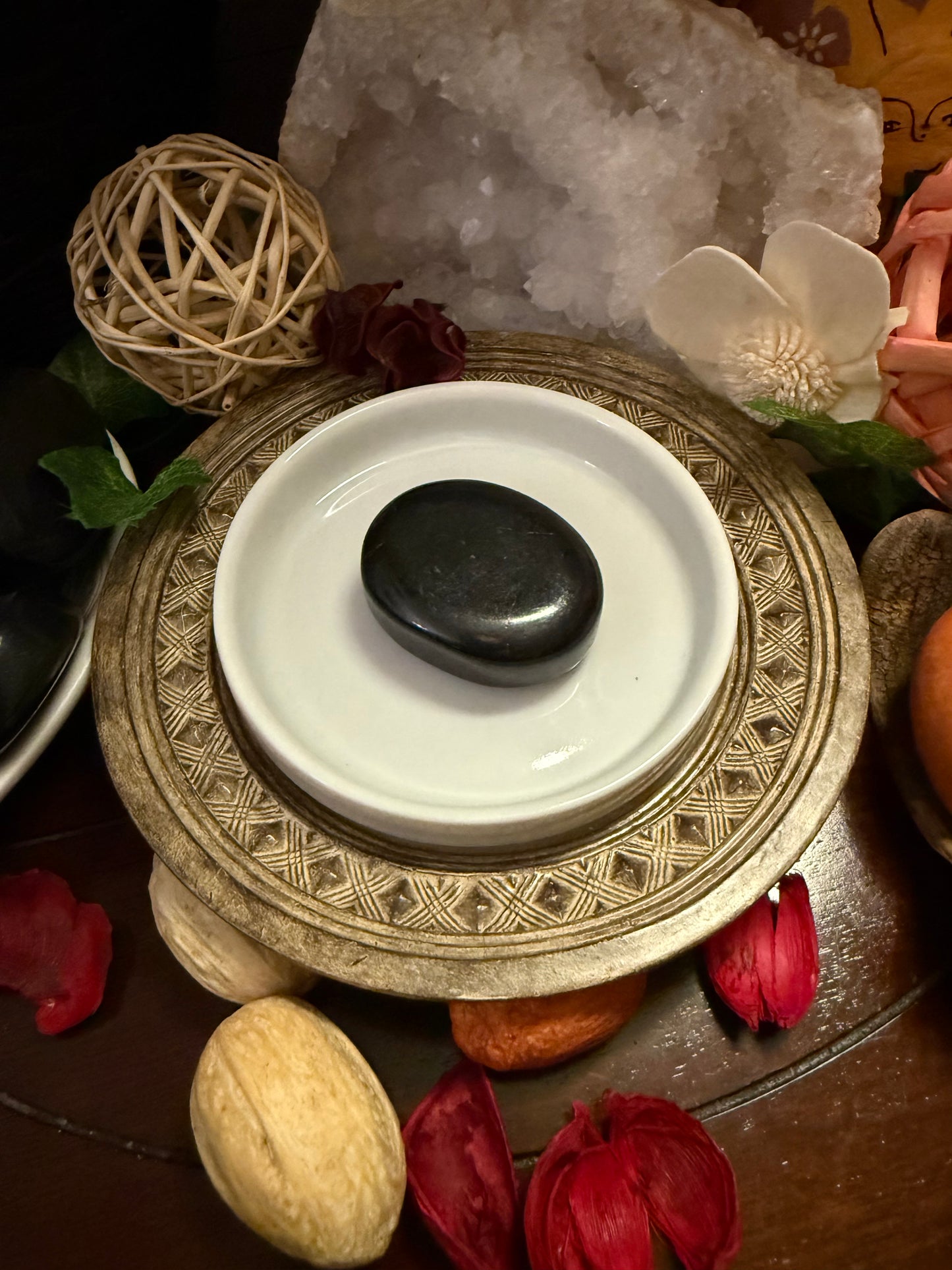 Decorative setting with a white dish, black stone, and various items on a dark surface.