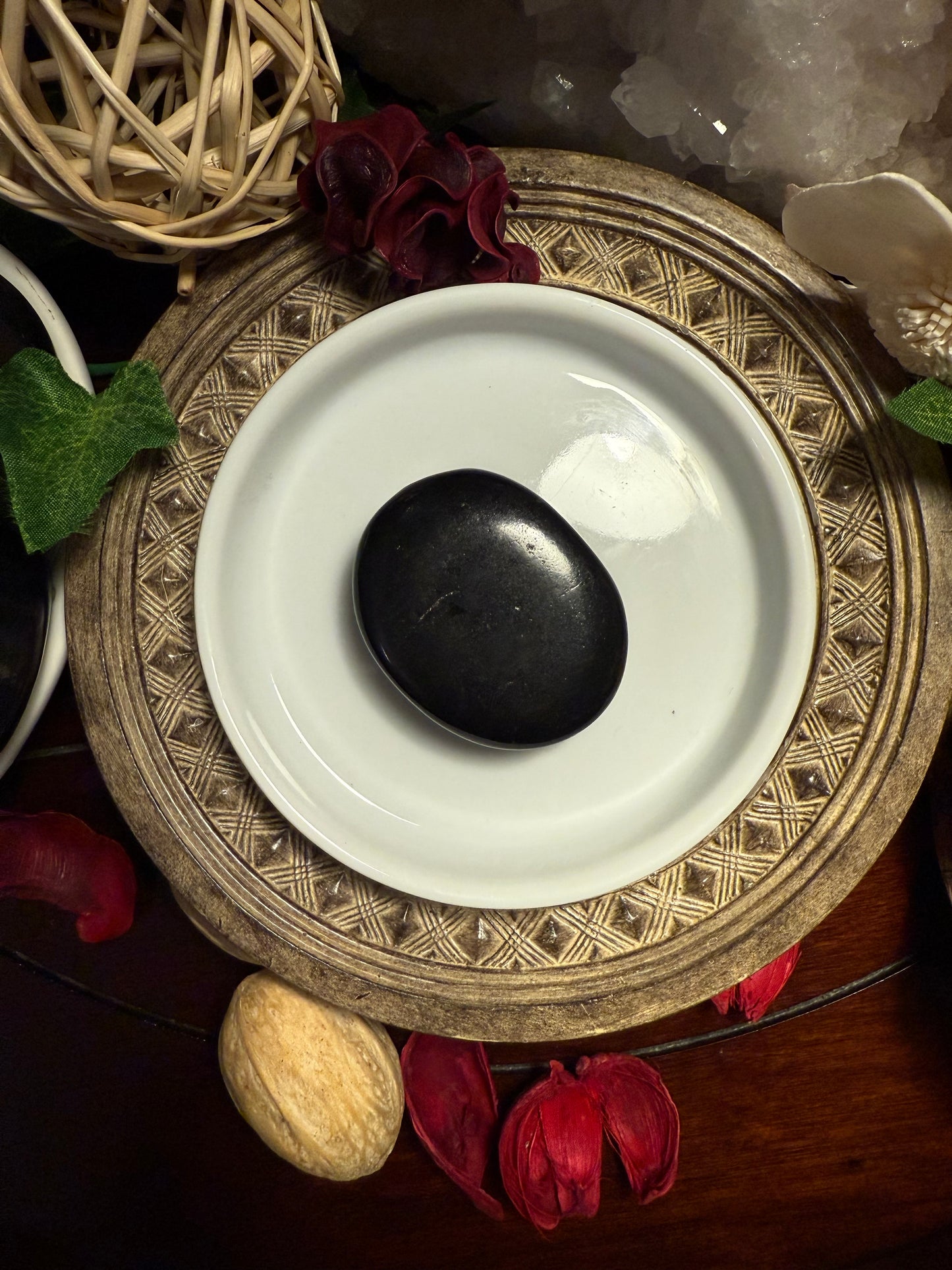Decorative setting with a white dish, black stone, and natural elements on a wooden surface.