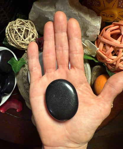 Hand holding a black stone with decorative items in the background