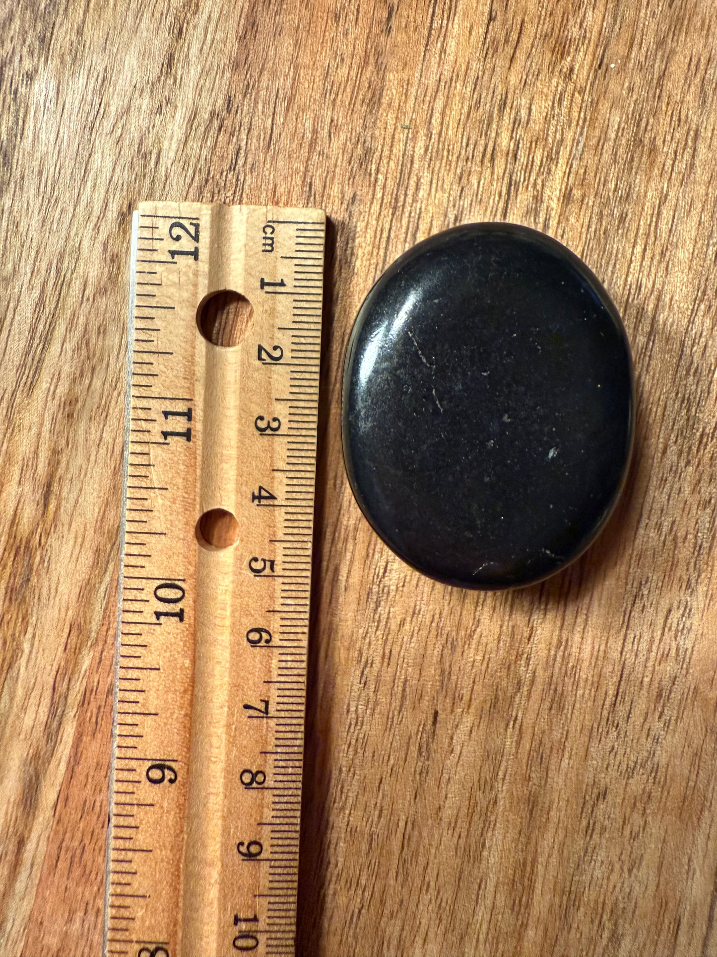 Black stone on a wooden surface with a ruler for scale