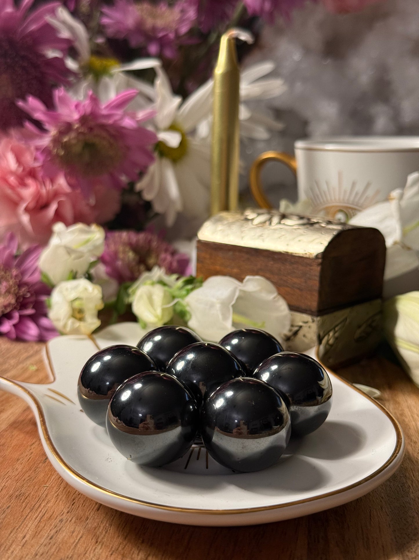 Black Magnetic Hematite Spheres on a white plate with flowers and a teacup in the background