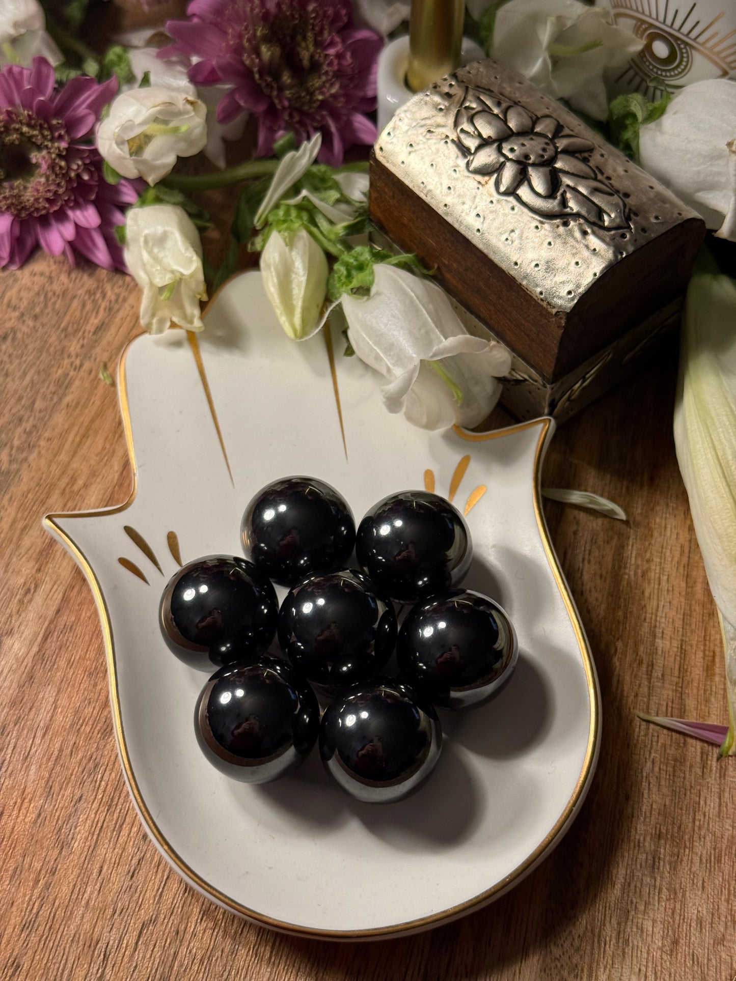Decorative dish with black Magnetic Hematite Spheres on a wooden surface with flowers in the background