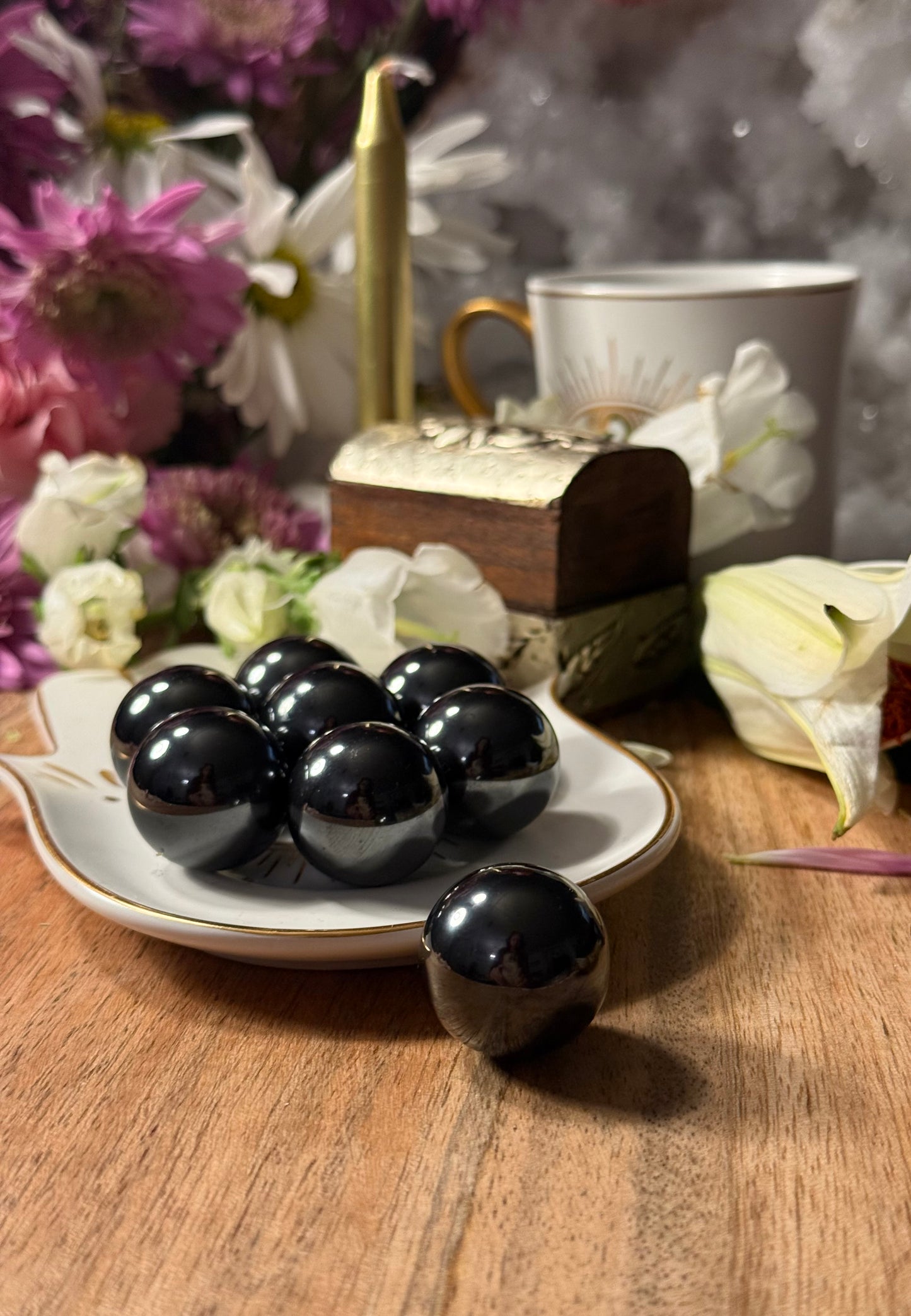 Black Magnetic Hematite Spheres on a plate with flowers and a teacup in the background