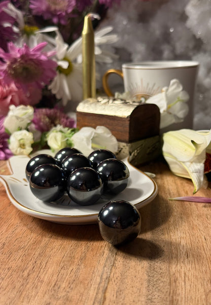 Black Magnetic Hematite Spheres on a plate with flowers and a teacup in the background