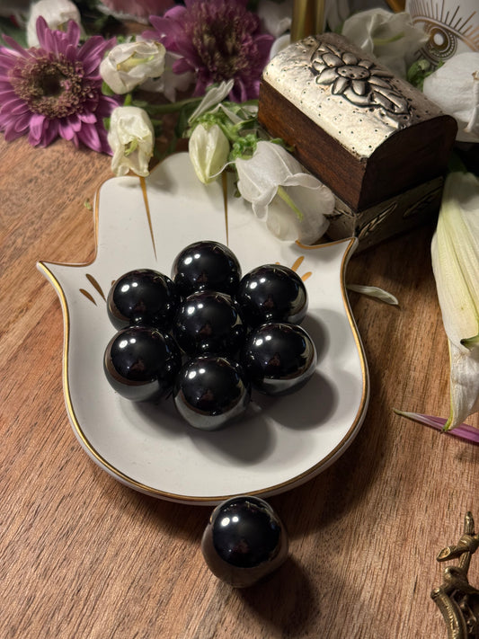 Decorative dish with Magnetic Hematite Spheres on a wooden surface with flowers.