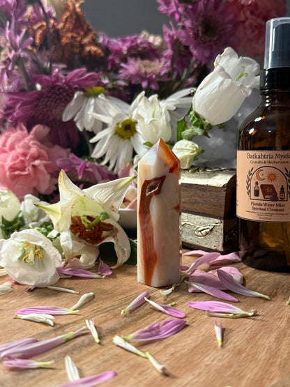 Carnelian Agate Crystal Point, essential oil bottle, and flowers on a wooden surface