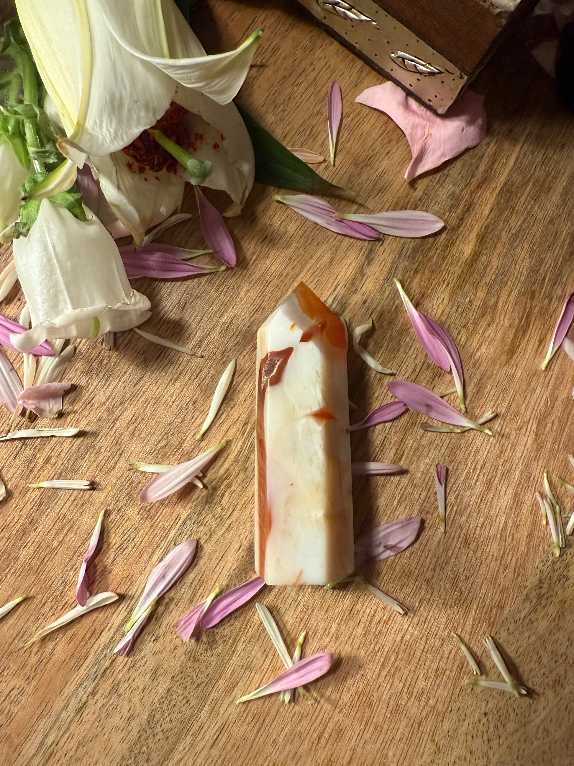 Carnelian Agate Crystal Point on a wooden surface with flower petals