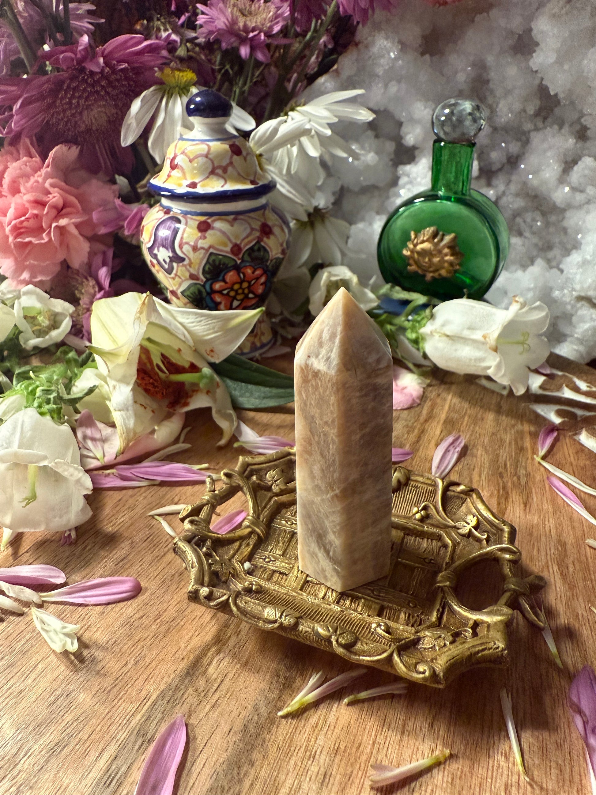 Decorative setting with a crystal on a brass stand, flowers, and a green bottle.