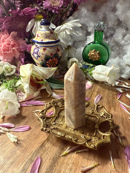 Decorative setting with a crystal on a brass stand, flowers, and a green bottle.