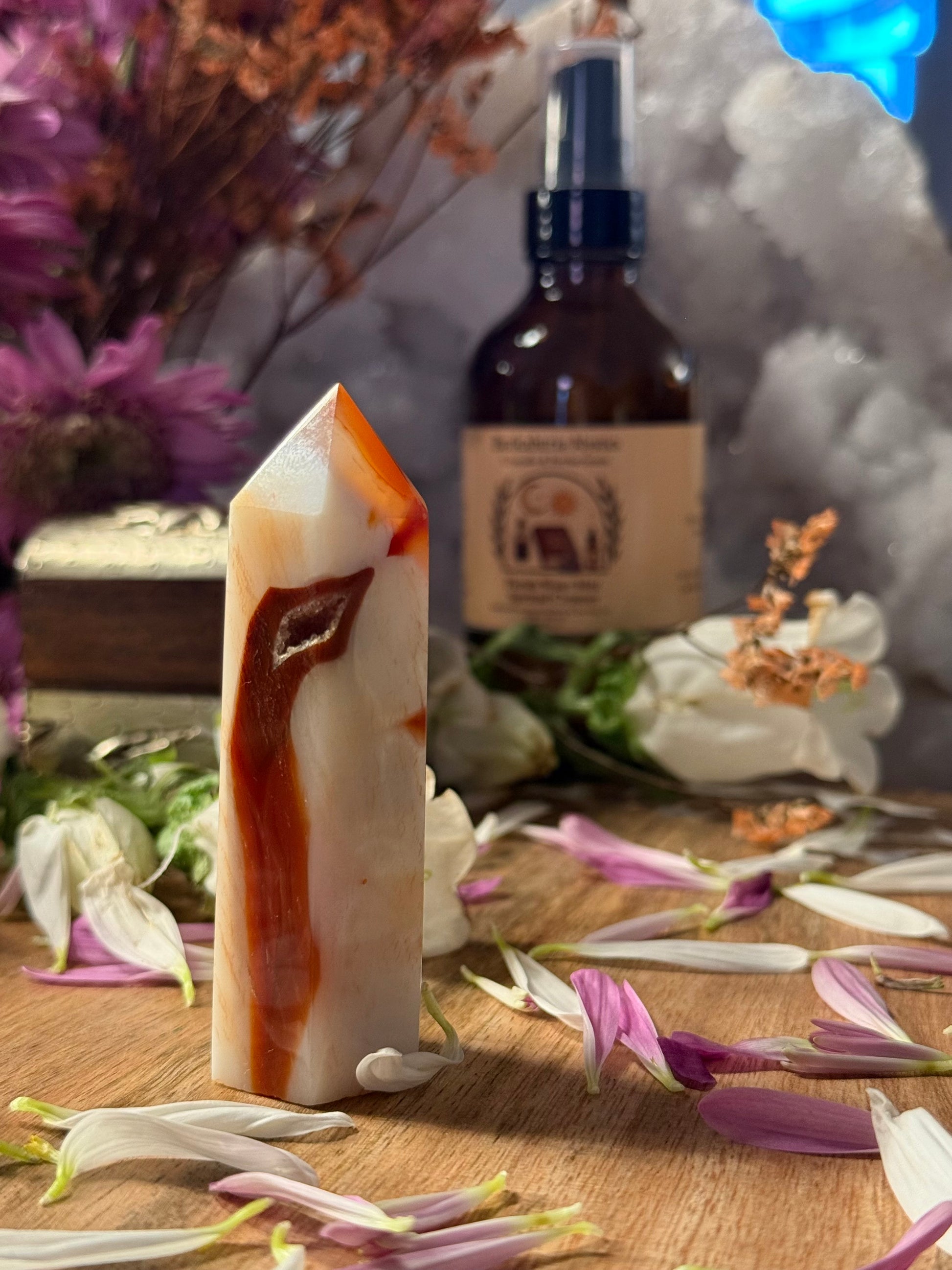 Carnelian Agate Crystal Point with a bottle of essential oil on a wooden surface with flowers and dried plants.