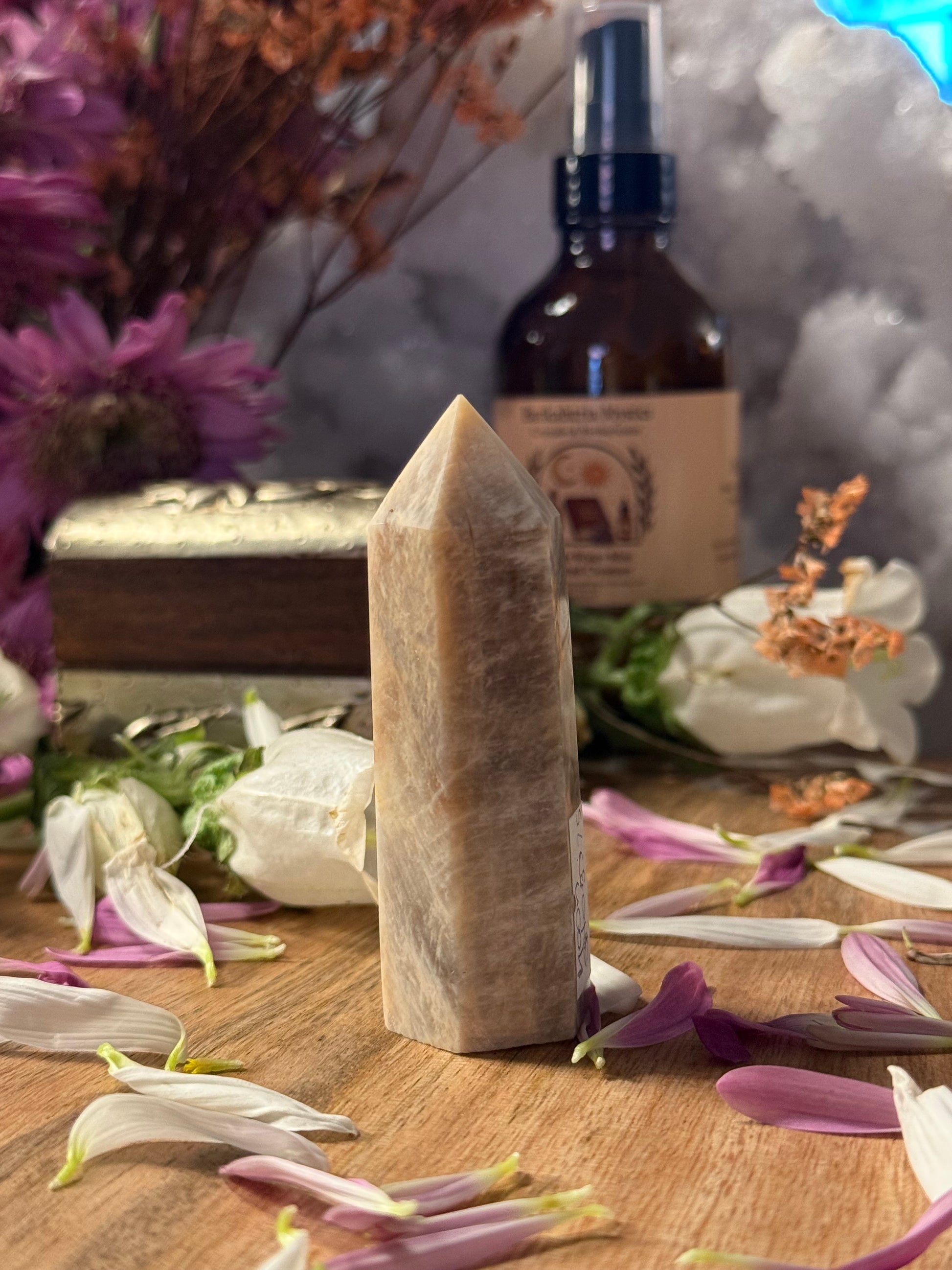 Crystal point on a wooden surface with flowers and a bottle in the background
