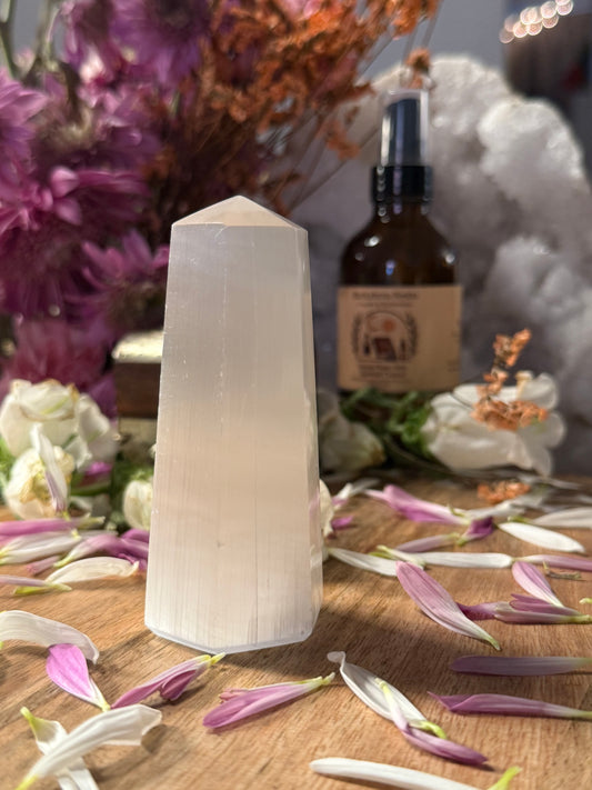 Selenite tower on a wooden surface with flowers and a bottle in the background