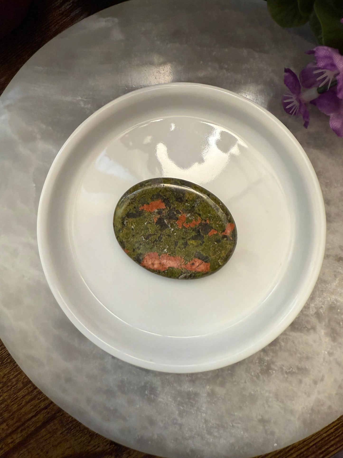 Decorative stone on a white dish with a purple flower in the background