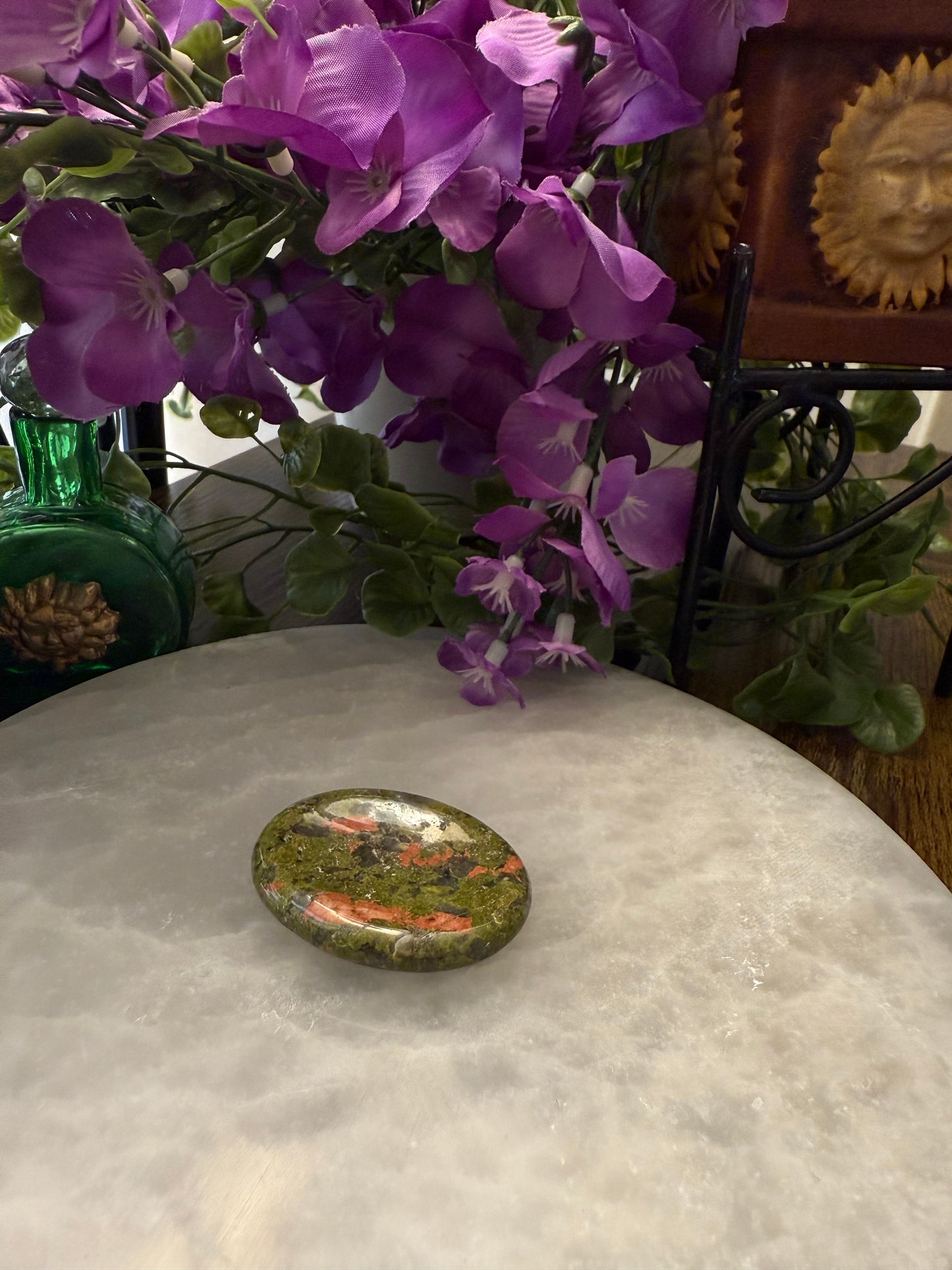 Purple flowers on a white surface with a decorative stone and green vase in the background
