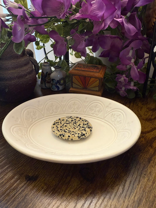 Decorative plate with a Dalmatian Jasper Worry Calming Stone on a wooden surface with purple flowers in the background