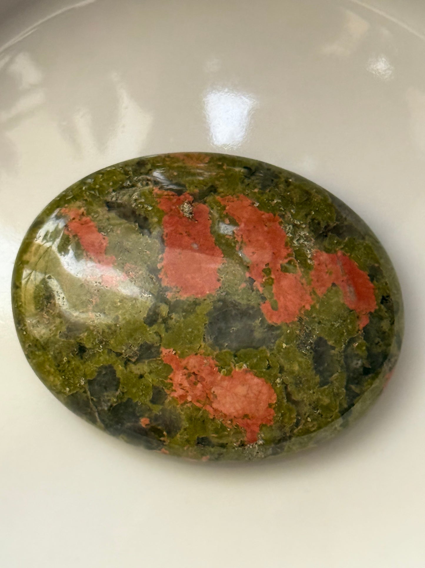 Oval-shaped stone with red and green patterns on a white background