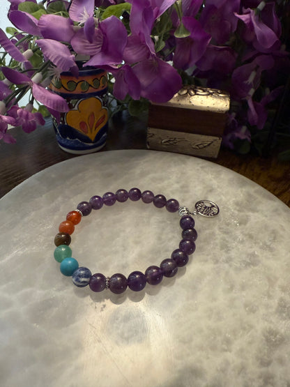 Amethyst Chakra Balance Bracelet on a marble surface with purple flowers in the background