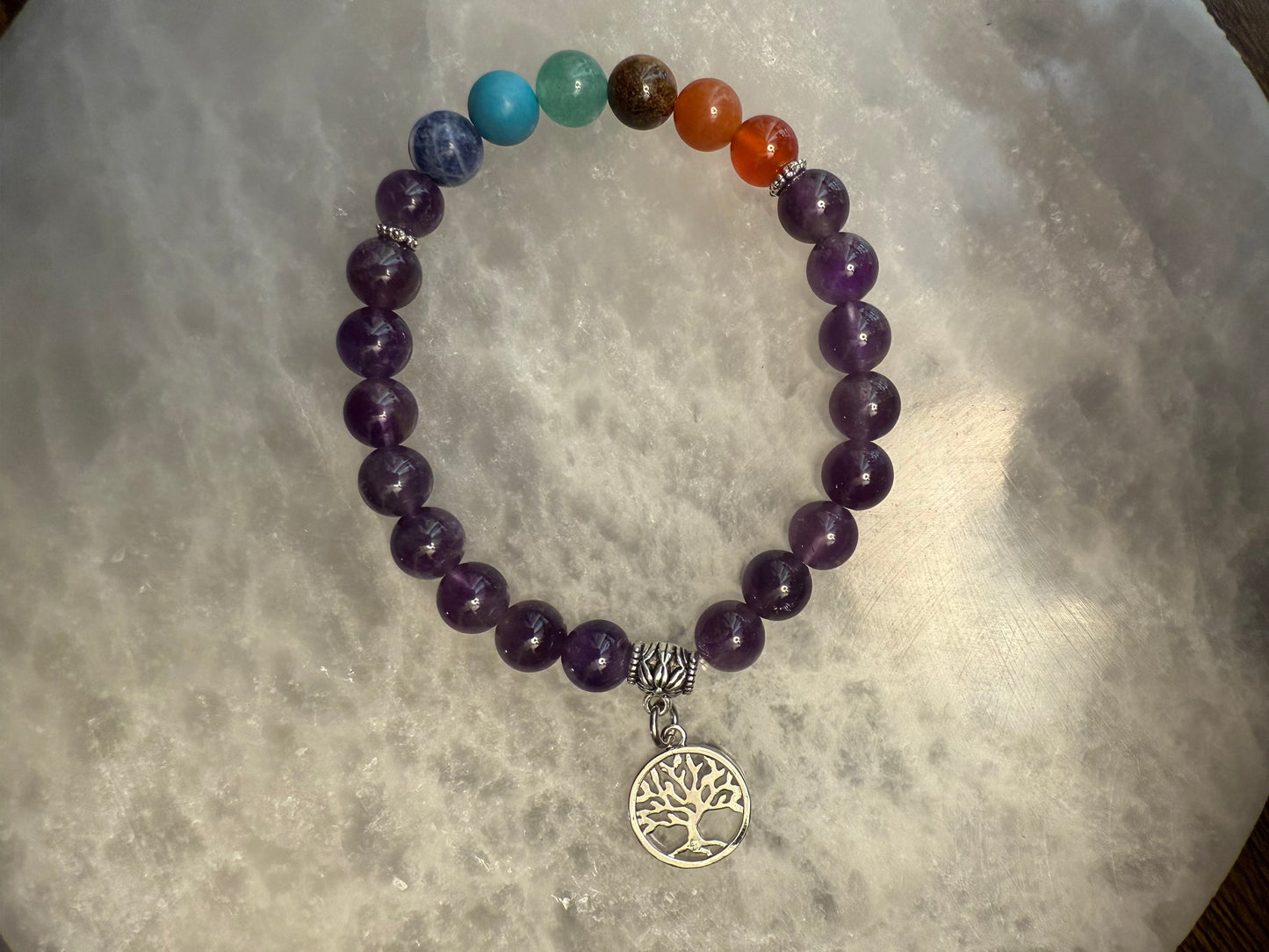 Amethyst Chakra Balance Bracelet with a tree of life charm on a textured surface