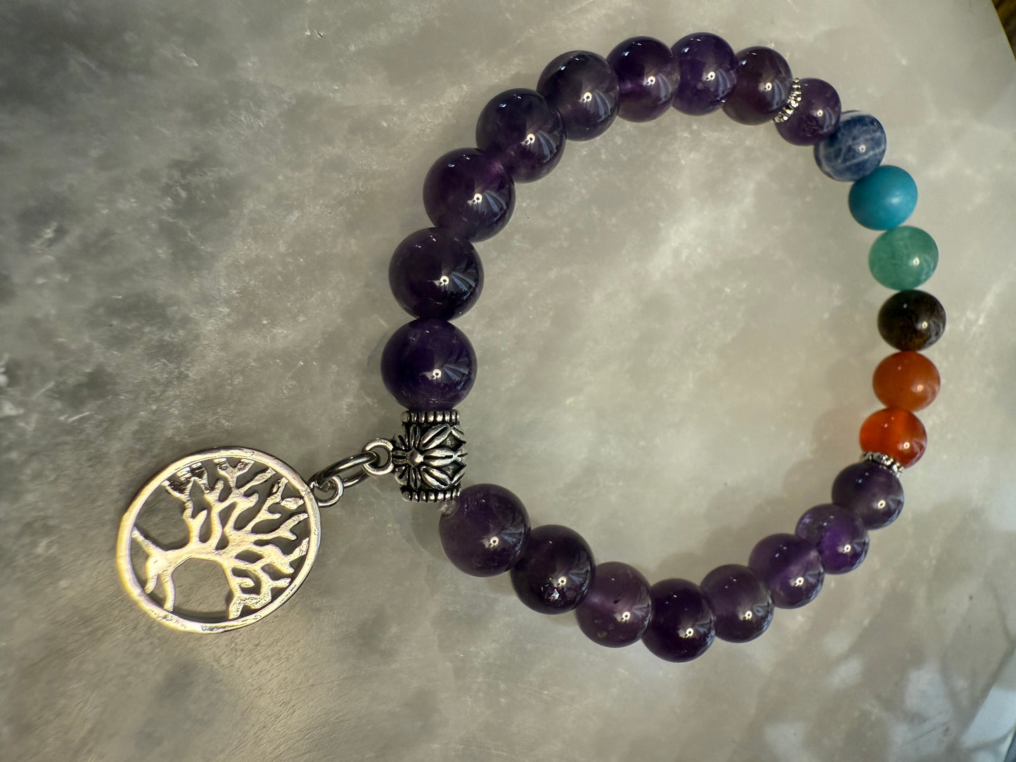 Amethyst Chakra Balance Bracelet with a tree of life charm on a gray surface
